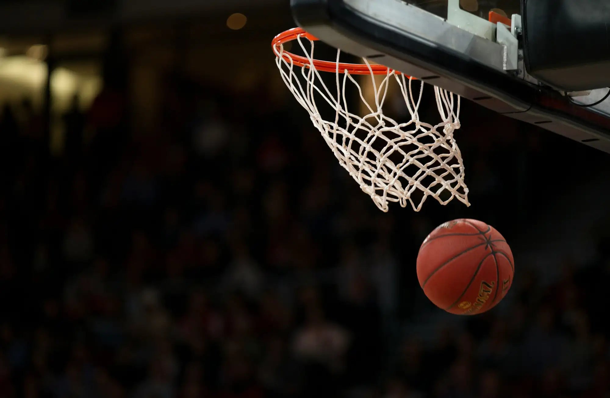 A red basketball with black seams is suspended in mid-air just below a white netted hoop.