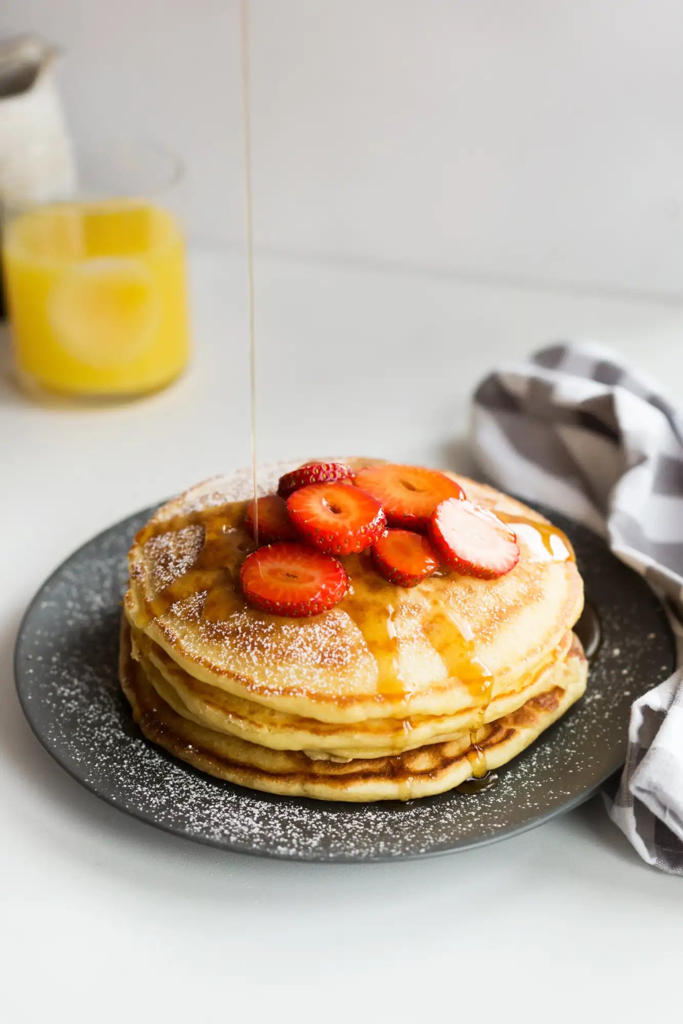 Stack of golden pancakes topped with sliced strawberries and drizzled syrup.